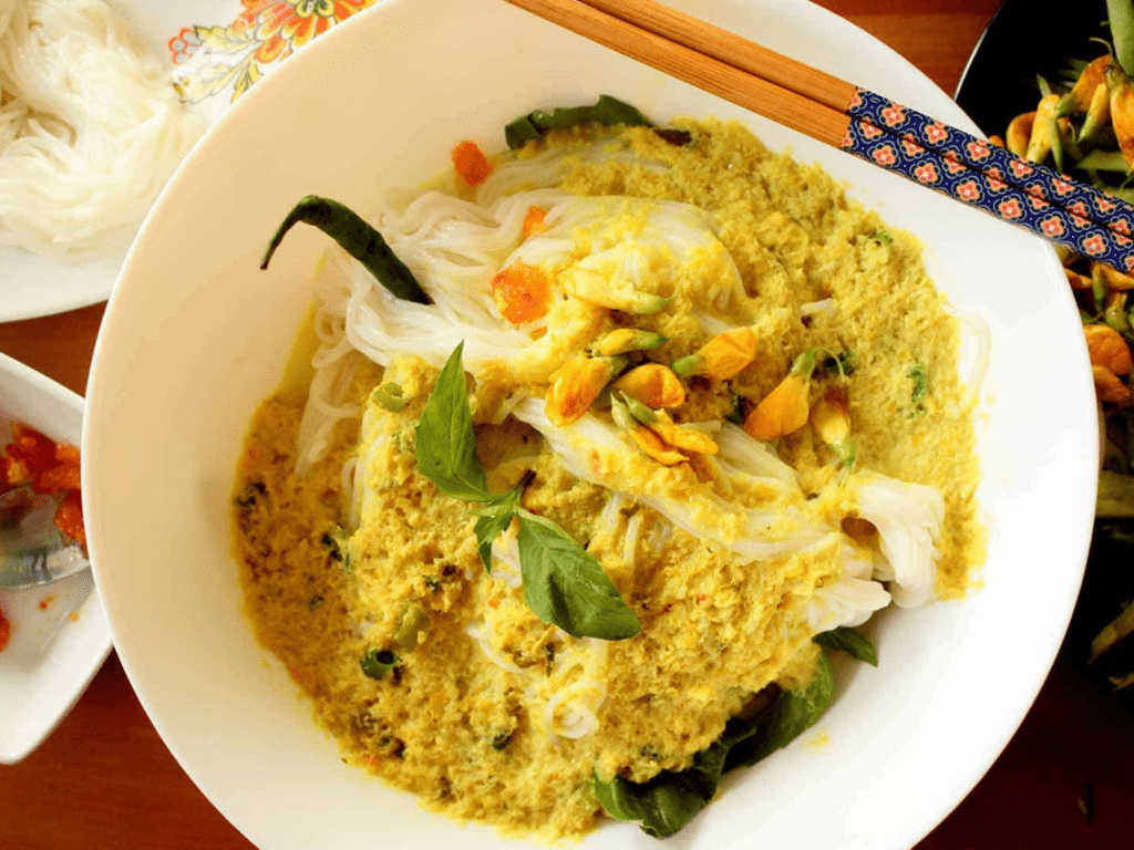 A bowl of Cambodian Nom Banh Chok, featuring rice noodles with green curry sauce, fresh herbs, and edible flowers. A signature dish in Cambodia travel guide recommendations.