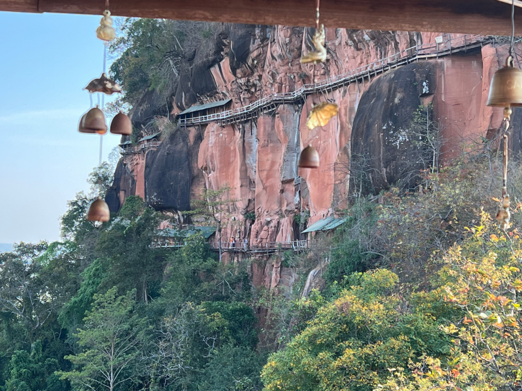 Hidden Thailand: A breathtaking view of Wat Phu Tok’s wooden walkways from a temple balcony, Unusual places in Thailand: Cliffside pathways of Wat Phu Tok framed by wind chimes, Hidden gems in Thailand: The adventurous wooden walkways along the cliffs of Wat Phu Tok, Best secret spots in Thailand: A scenic viewpoint overlooking the rock temple walkways, Off-the-beaten-path Thailand: Suspended wooden bridges on the cliffs of Wat Phu Tok