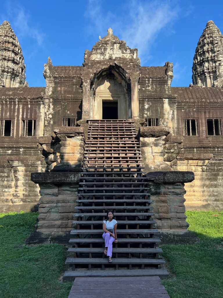 A traveler sitting on the steps of Angkor Wat in Siem Reap, Cambodia, showcasing the impressive architecture of this historic Khmer temple.