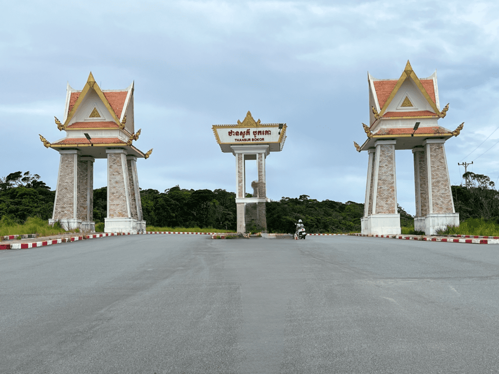 Traditional Khmer-style entrance gate to Thansur Bokor National Park in Cambodia with a motorbike passing through.