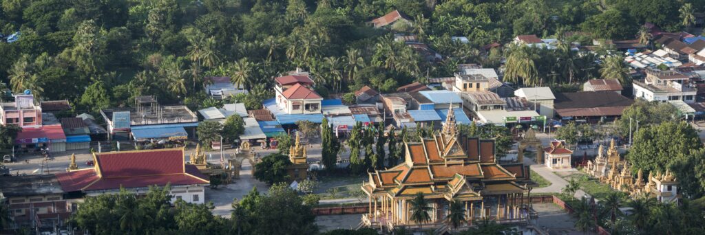 Aerial view of Battambang, Cambodia, featuring a traditional Buddhist temple with golden rooftops, surrounded by lush greenery, local markets, and Khmer-style houses. A must-visit destination for cultural tourism in Cambodia.