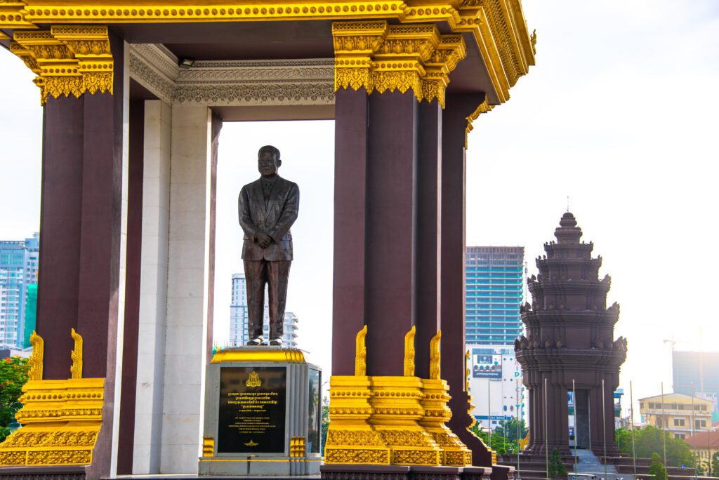 Bronze Statue of Norodom Sihanouk, Phnom Penh, Cambodia – A striking bronze statue of Norodom Sihanouk under a golden pavilion in Phnom Penh, Cambodia, with the Independence Monument in the background. A must-visit historical landmark in the capital.