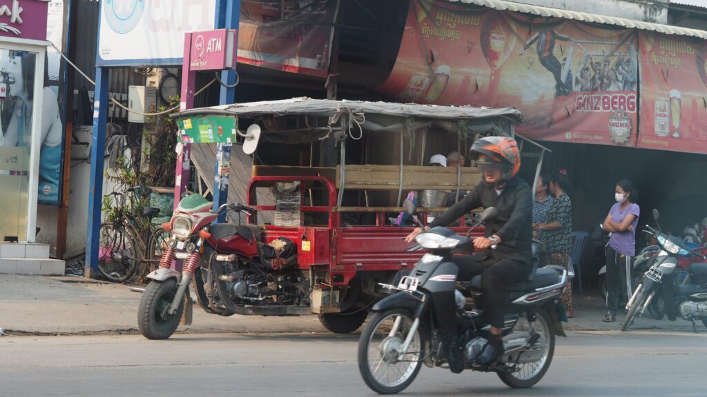 Busy Phnom Penh Street Scene with Motorbikes and Tuk-Tuks – A lively street in Phnom Penh featuring a tuk-tuk, motorbikes, and a busy market atmosphere. A typical scene showcasing Cambodia’s vibrant street life.