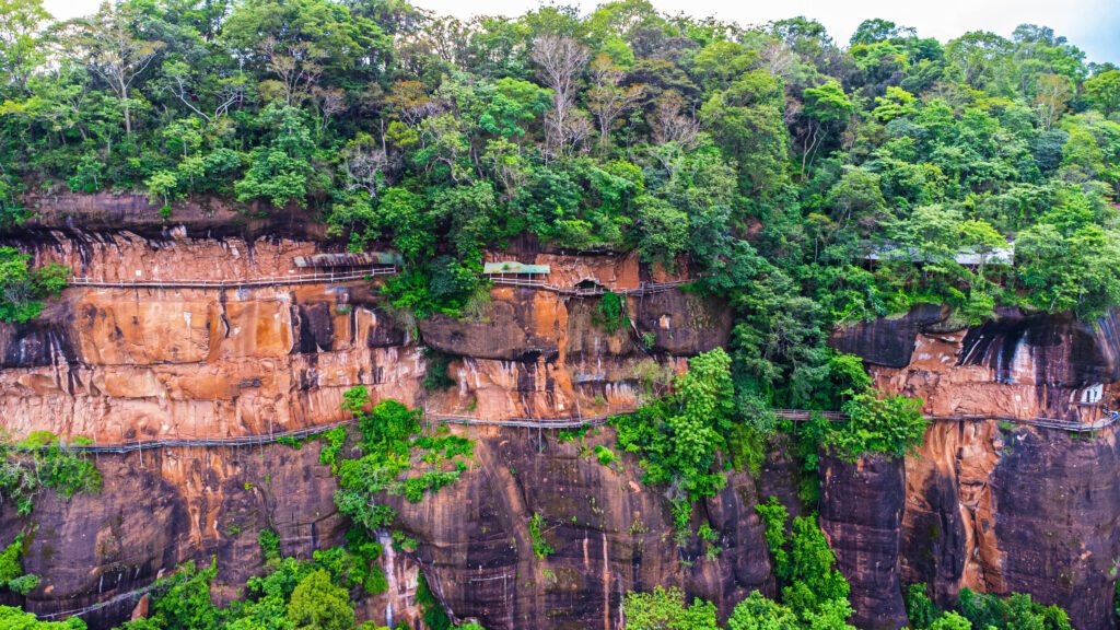 Hidden Thailand: Stunning cliffside temple walkways at Wat Phu Tok, Unusual places in Thailand: Wat Phu Tok’s wooden walkways suspended on a sheer rock face, Hidden gems in Thailand: A breathtaking aerial view of Wat Phu Tok’s dramatic cliffs, Best secret spots in Thailand: The isolated mountain monastery of Wat Phu Tok, Off-the-beaten-path Thailand: Adventurous wooden paths winding along Wat Phu Tok’s cliffs