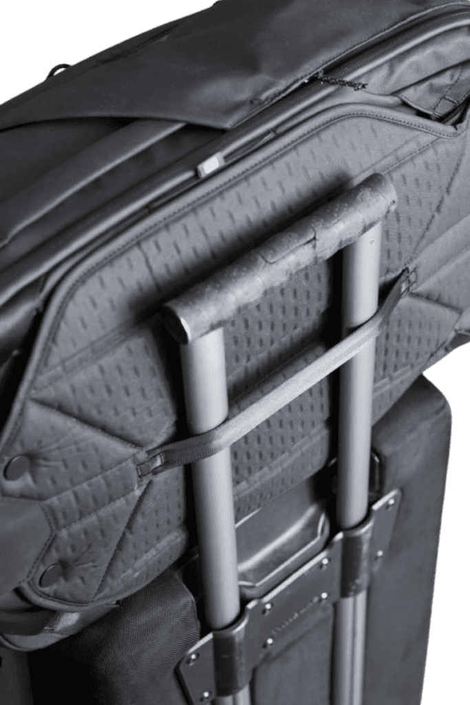 Travel backpack attached to a rolling suitcase handle, illustrating its convenient luggage pass-through feature.
